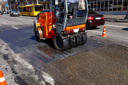 筑路工一条重橙色振动横轴压板在一条有交通锥形栅栏的市区街道上铺平一段路面用复印空间图像制对市街路段道进行修补理铺沥青图片