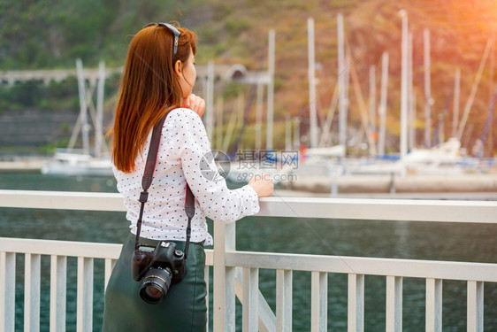 时尚皮肤奢华一位漂亮的读数头女孩带着相机看阳光下的码头女人准备在加那利群岛拍摄旅行照片游艇在背景上柔和聚焦游艇在背景上的软焦点图片