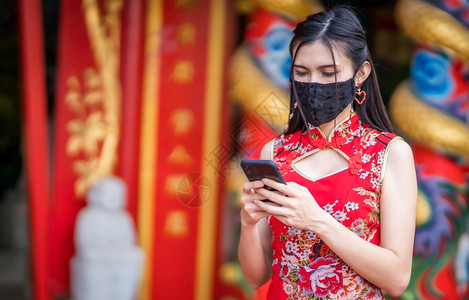 亚裔年轻女身着传统红青山长相衣装饰并戴保护面具和智能手机用于新年节圣迹防止COVID19传播的中华新年节吸引人的们保持图片