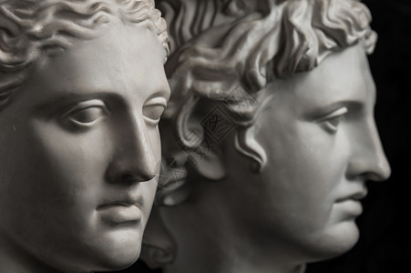 黑色的罗马智慧古代阿波罗和戴安娜雕像的白色石膏复制品供艺术家在深色纹理背景上使用雕像脸的石膏塑古代像阿波罗和戴安娜头的石膏复制品图片