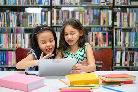 女孩们观看两个快乐的小可爱女孩在学校的图书馆里玩电脑平板游戏教育和自学无线技术概念人们的生活方式和友爱孩子都喜欢听人说教学生们讲图片