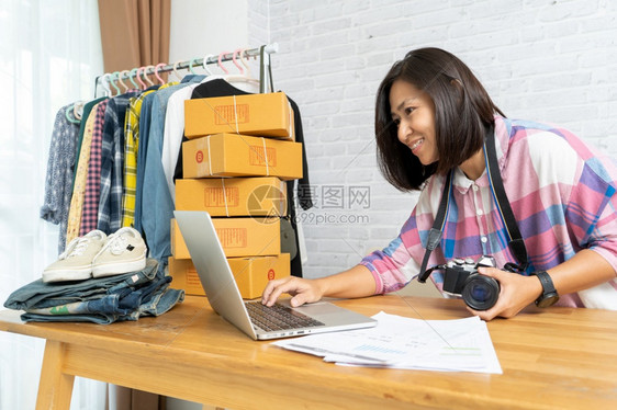 在线的中小企业交货在网上销售笔记本电脑的亚洲妇女工作开始创办小企业主拿着相机准备接受产品电子商务理念的概c电子商业概念图片