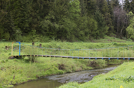 在树林中挂着一座悬吊桥横跨山河高上的悬浮桥在明亮的绿林喀尔巴阡山脉乌克兰森林中挂着悬吊桥跨越山河穿过越木头水平的布罗德高清图片素材