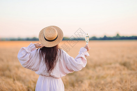 秋天穿着装和戴草帽手握着葡萄玻璃的美观小麦田中女孩的景象穿着草帽手拿成熟小麦的美貌佳人花束丽的图片