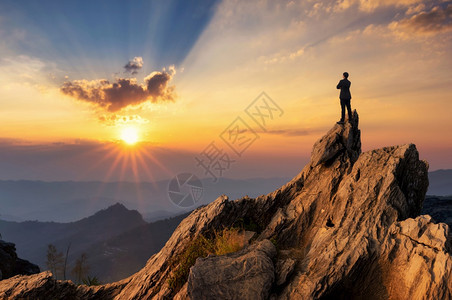 年轻商人穿着舒适的便衣夹克站在山峰顶上拥抱胸前期待未来成功竞争和领袖概念展望未来期竞争和领袖概念战略成功的解决方案背景图片