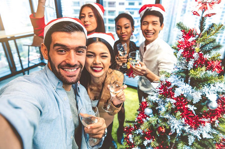 圣诞节前夕公司的在工作办室多种族样青年商业团体用手机相自拍的男女混合种族朋友庆祝圣诞快乐和20年新欢庆晚会的工作自我肖像在工作办图片