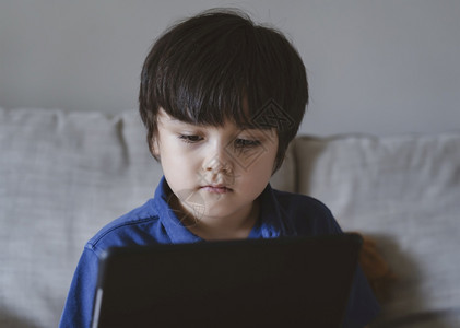 自在距离搜索学校儿童使用平板电脑做功课儿童以思考的面孔看数字平板电脑青年男孩在触摸垫上看漫画正常生活靠在线学习维持远程教育图片
