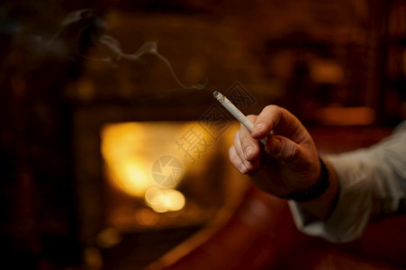 男手拿着烟有丰富的办公室内地有背景吸烟文化的壁炉特殊口味的抽烟文化家里的抽烟者闲暇时间男手拿着香烟有背景壁炉富裕房间扶手椅图片