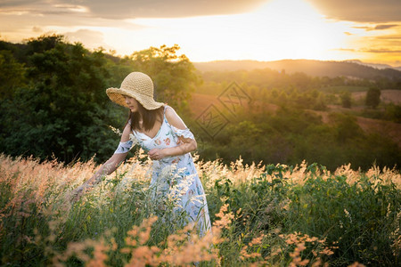 假期女孩戴帽子穿白色衣服站在草地中间穿着美丽的白花在太阳下定时间在山上心情放松和快乐的山上她戴着帽子穿白色裙站在草丛中温暖的花朵图片