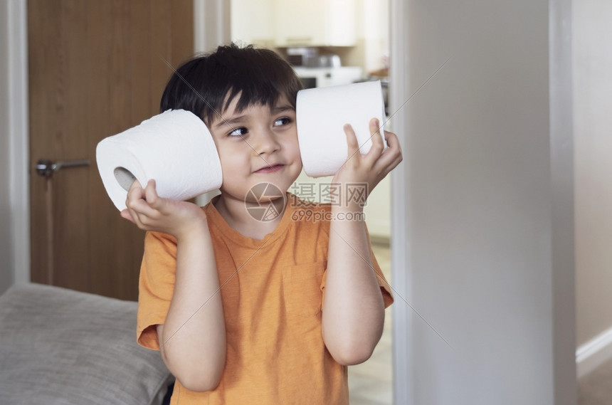 锅消化他的快乐年轻男孩带着微笑的脸玩卫生纸孩子把厕所卷放在耳朵上儿童持有两个白色组织儿童保健概念的图片
