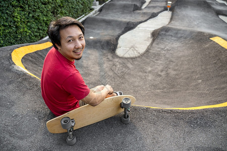 轮子超速亚洲男与冲浪skate或滑板一起坐在轮冰公园中日出时间超过浮轮曲线外形运动健康和时尚等相光模糊点的日出时间风险图片