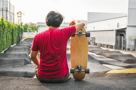 或者亚洲男子与冲浪skate或滑板一起坐在轮冰公园中日出时间超过浮轮曲线外形运动健康和时尚等相光模糊点的日出时间泵道锻炼图片