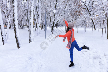 假期树木一名年轻美丽的女士穿着明亮珊瑚夹克和蓝色牛仔裤在冬季沿着雪覆盖的童话仙女公园小巷行走扔了大雪球一名年轻美丽的女士在冬天沿图片