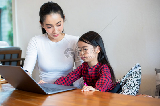 无线的亚洲母亲正在教女儿阅读一本书并使用笔记本和技术在家庭学校放假期间进行网上学习教育概念和家庭活动教育概念与家庭活动利用笔记及图片