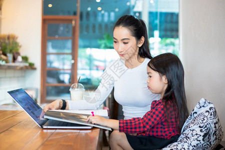 亚洲母亲正在教女儿阅读一本书并使用笔记本和技术在家庭学校放假期间进行网上学习教育概念和家庭活动教育概念与家庭活动利用笔记及技术开图片