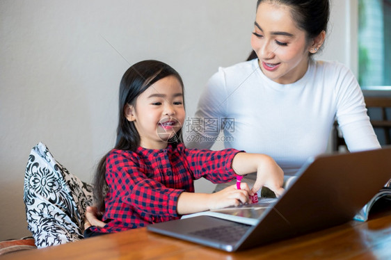 亚洲母亲正在教女儿阅读一本书并使用笔记本和技术在家庭学校放假期间进行网上学习教育概念和家庭活动教育概念与家庭活动利用笔记及技术开图片