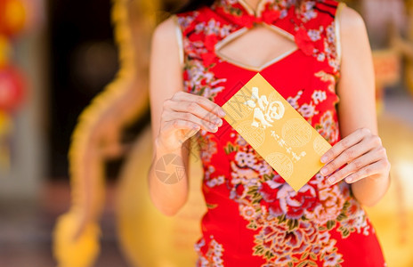 身着红色传统青山装饰的紧近亚裔年轻女子拿着黄信封上面写着中文字祝福是华元新年节的好运淑女手时尚图片