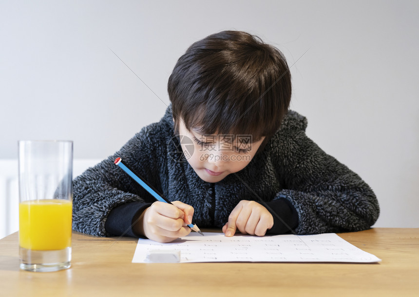 男生可爱的孩用笔写在白皮书上的纸学生在家时做拼写测试在家庭学校概念中生们做了拼写测试a独自的教育图片