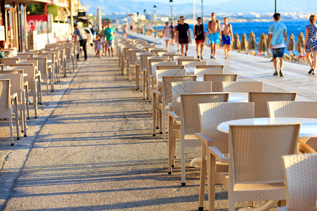 旅行海滩咖啡厅的桌椅位于海边休息的人和孩子们在海边走来去时都模糊不清用影印空间图像照海滩咖啡厅的桌椅与位于沿台阶一旁人们在蓝海附图片