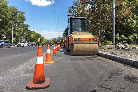 沥青构造车轮橙色公路锥体保护在城市街道上重振动压板的工作场所橙色公路锥体保护沿城市街道边缘的重型轮式紧压机以及图片