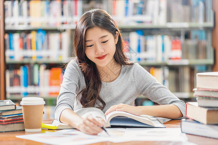 知识亚洲青年学生在大图书馆或群落阅读和做功课书架背景的木制桌子上有各种书本和文具回学校后读书架背景上的各种书籍和文体成人写作图片