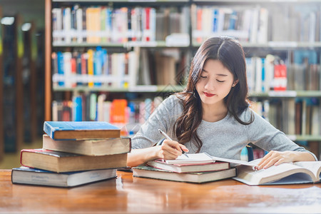 学术的内阁亚洲青年学生在大图书馆或群落阅读和做功课书架背景的木制桌子上有各种书本和文具回学校后读书架背景上的各种书籍和文体样的背景图片