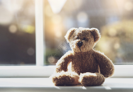 过敏在阳光的白天坐在靠近窗户的阳光日落下的高关键光亮可悲泰迪熊独自在家坐的孤褐熊社会不和概念留在家中和防止疾在儿童中的传播打喷嚏图片