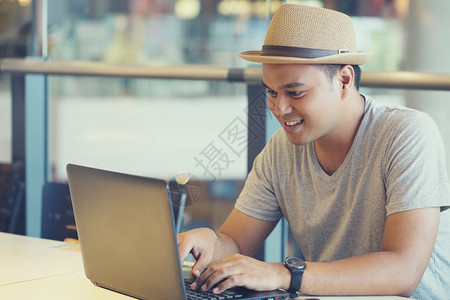 在一个咖啡店后视窗里工作在笔记本电脑上工作的男青年嬉马子在办公桌用笔记本电脑忙着做生意的人手在木制桌子的电脑上打字年轻男学生的教图片