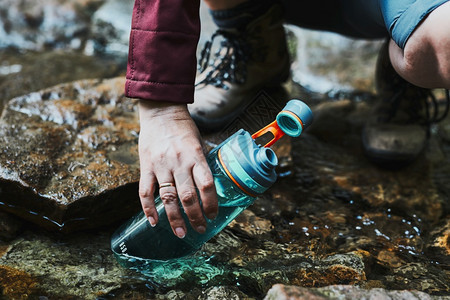 游客在山上漫步时用纯净的水瓶装河流里的水图片