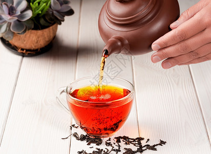 混合泡茶的过程仪式从一个粘土茶壶红被倒入一杯玻璃新鲜酿成的黑茶温暖柔软灯光白木背景密闭抽烟光束图片
