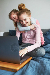 人们在COVID19隔离期间孙女和她的妹在家里笔记本电脑上与祖父母进行视频通话女孩坐在电脑前的床上更年轻孩子们图片