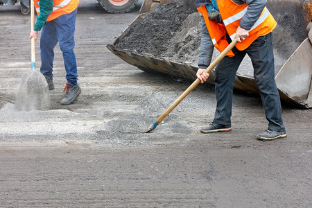 巷道工作灰色的身穿明橙反射背心的运输工人在清理公路上的旧沥青之后为修车准备旧路面并将道残骸清除成一个平板桶然后从公路上清除旧沥青图片