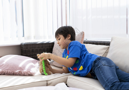 学校儿子夏天坐在沙发上与狗玩具耍面脸快乐的男孩玩软具或在暑假放学时间家松积极儿童概念在沙发上躺的短快乐孩子图片