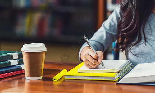 学校习亚洲青年生在大图书馆或同事的写家庭作业各种书本和文具在架背景上用木制咖啡杯放在板桌上Backtoschool内阁图片
