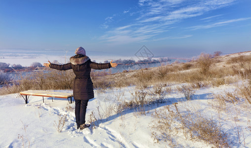 乡村的乌克兰一位身处冬日升照光的年轻女子迎接南虫河岸的黎明站在木板凳附近的一座山丘上望着宽阔的手臂伸展距离一位年轻女子在阳光灿烂图片