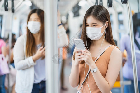 泰国在Covid19爆发感染和大流行病概念的都市旅行时身戴外科面具并通过地铁火车智能手机监听音乐的亚洲女青年乘客在Covid19图片