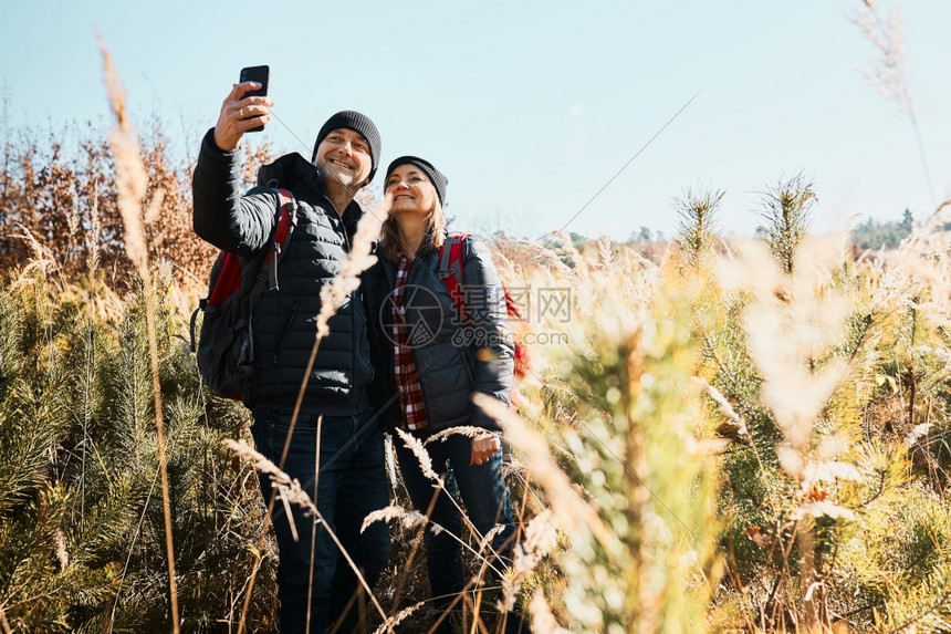 在度假旅行时抱着一对夫妇自拍乘带背包的希克人前往山上们在阳光明媚的白天穿过高草地走在原上的小路享受与自然相近的闲暇时间问候活动沿图片