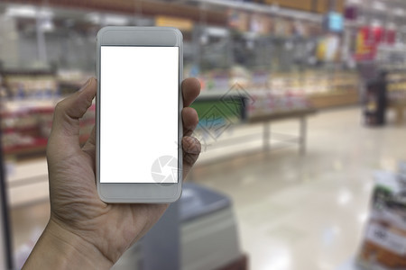 人们手持智能机白色空屏幕覆盖模糊的超市和购物商场内地背景零售店供产品显示时使用面纱电话信息图片