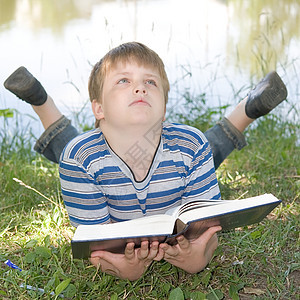 男孩读一本大书男性场地草地文学页数眼睛家庭季节公园教育图片