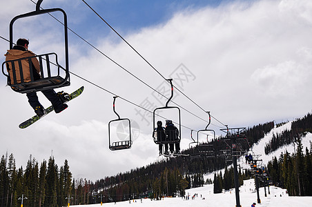 滑雪度假胜地的滑雪者享受森林树木娱乐松树乐趣升降椅白色天空缆车图片