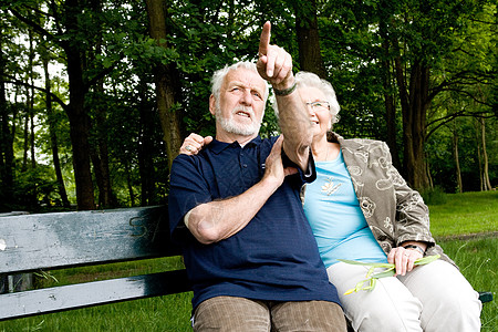 一对老夫妇坐在公园长椅外的一对夫妇背景