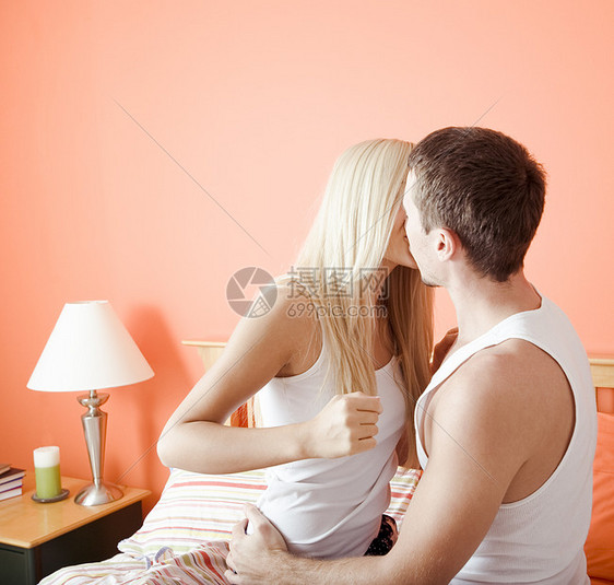 年轻夫妇跪在床上亲吻上男人床头柜影棚女士棕色公寓房子男性图书头发图片