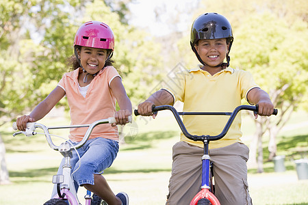 哥哥和姐姐在户外的自行车上微笑着笑女孩相机乐趣男生享受男性女性农村骑术头盔图片