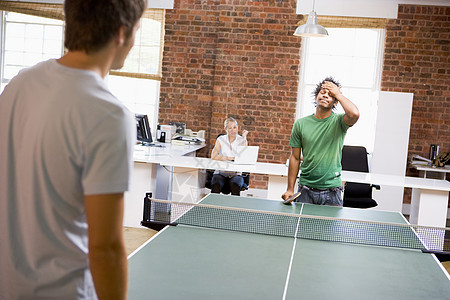 两名男子在办公室空间打乒乓球同事桌子男人欢呼乒乓竞赛优胜者女性男性中年图片