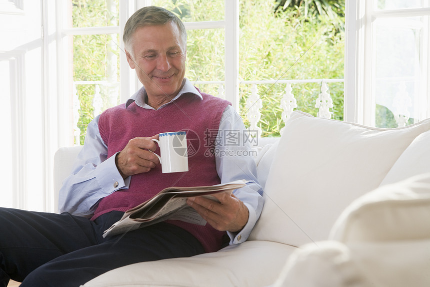 在客厅的男人 咖啡阅读报纸笑着的休息室水平长度女性沙发时事相机一杯茶微笑长椅图片