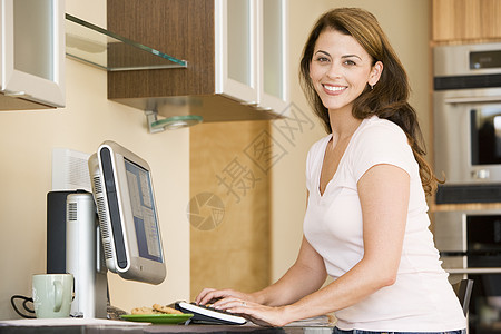 厨房里的女人带着电脑微笑中年咖啡水平饼干互联网拉丁混血儿成人杯子办公图片