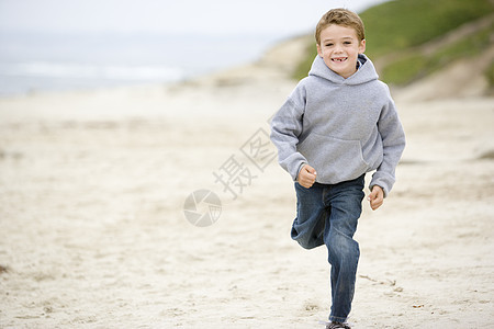 在海滩上微笑的年轻男孩跑步海岸活力海洋相机孩子们小男孩季节衣服男性图片