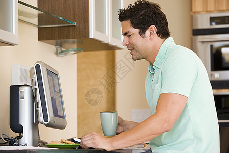男人在厨房里用电脑和微笑的咖啡喝咖啡图片