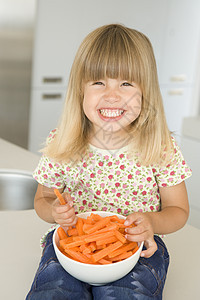 在厨房吃胡萝卜棒的年轻女孩笑着生产蔬菜零食小吃孩子一个女孩饮食健康饮食女性儿童图片