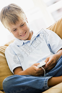 在客厅的年轻男孩 与MP3玩家微笑耳机享受孩子们孩子设备沙发音乐音频座位椅子图片